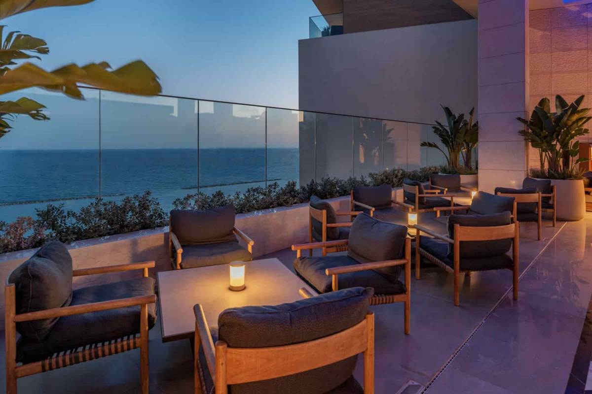 The Rooftop Bar at Amara at dusk, with low armchairs, lanterns and a glass balustrade above the sea
