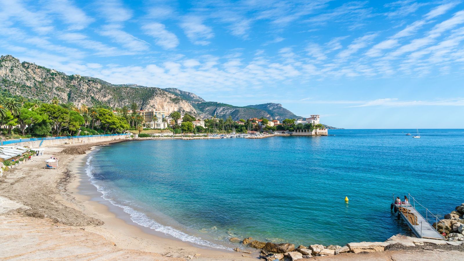 The beach on the Baie des Fourmis at Beaulieu-sur-Mer, with clear water below the wooded shore