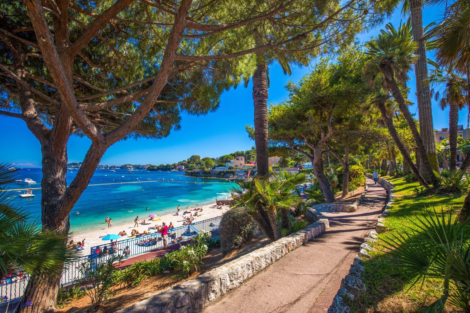 The seaside promenade at Beaulieu-sur-Mer under palms and pines, with the beach and clear water below