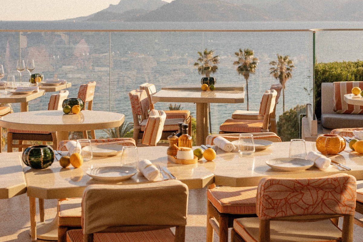 Tables on the Bella rooftop terrace on the eighth floor of the Hôtel Belle Plage, with palms and the sea below