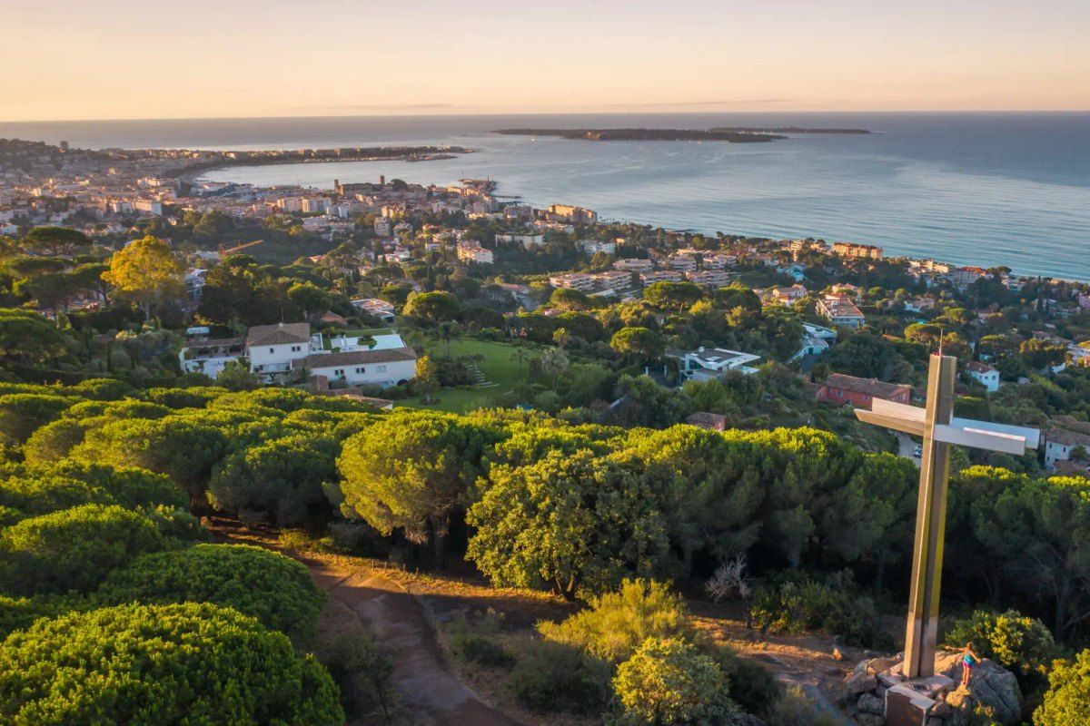 The steel cross at the top of the Croix des Gardes above pines, with Cannes and the sea below