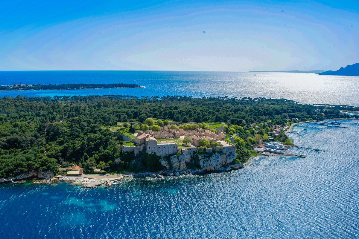 Aerial view of Île Sainte-Marguerite, its pine forest and rocky shore in the blue water off Cannes