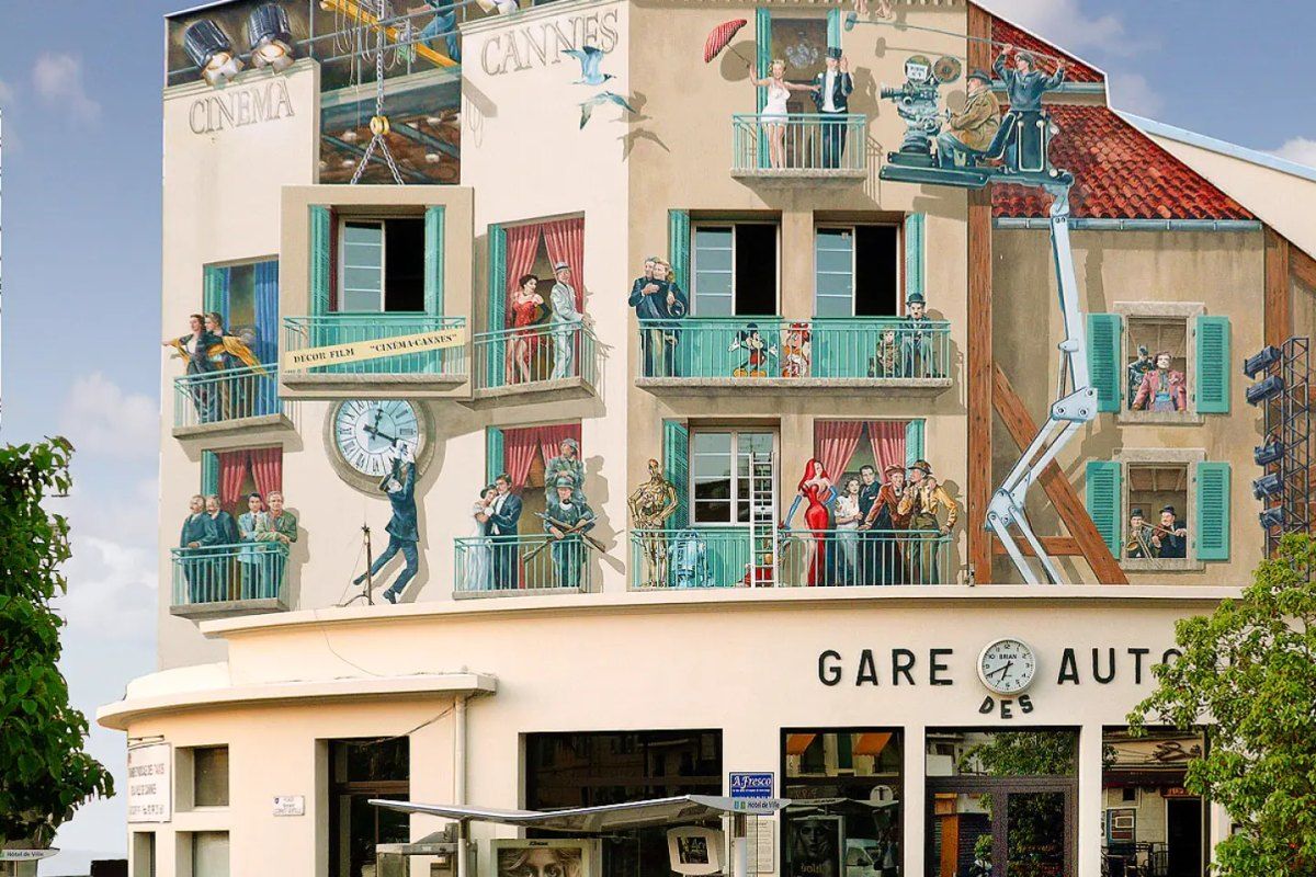 A trompe-l'oeil film mural covering a building above a garage in Cannes, with painted balconies and film stars