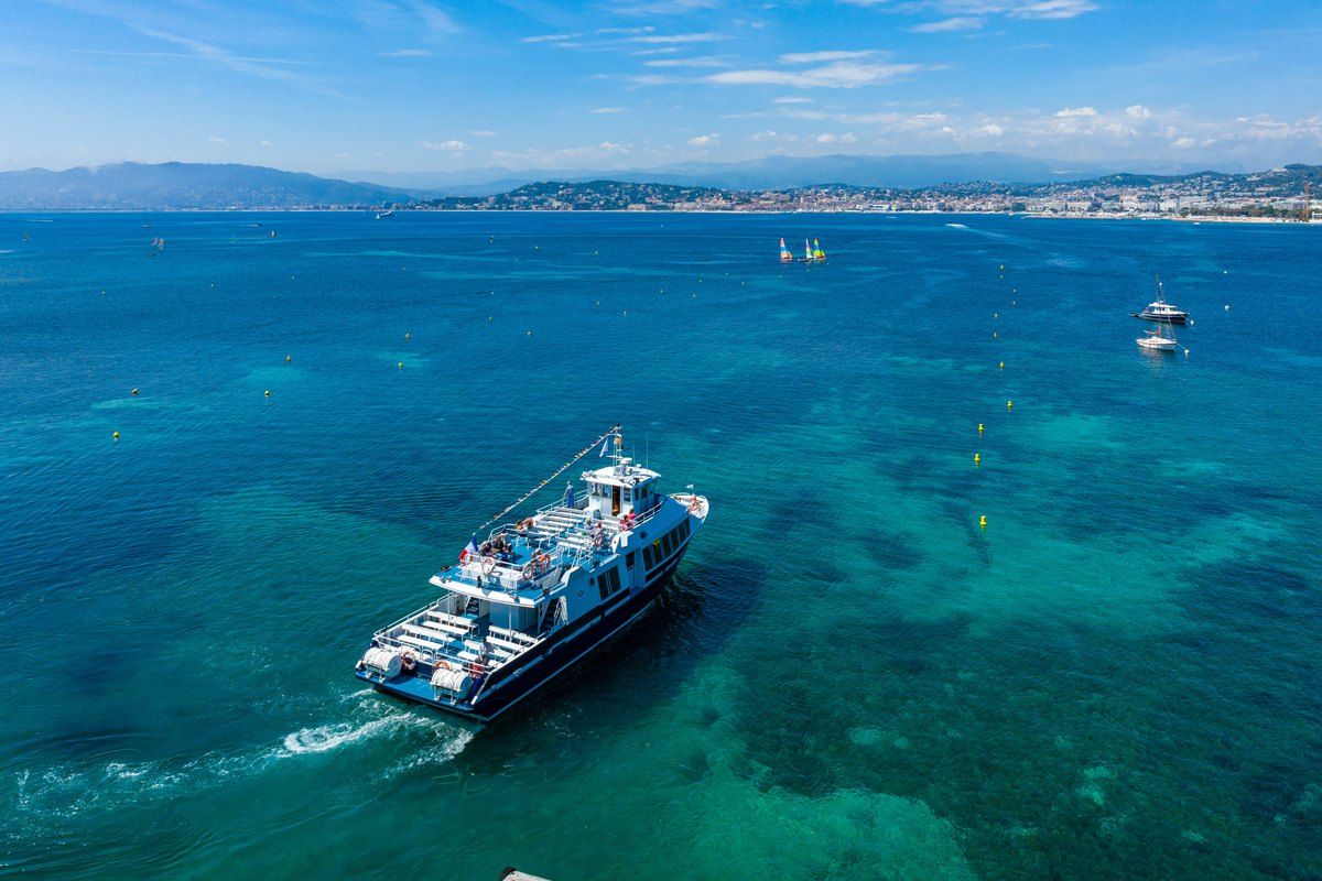 A Riviera Lines ferry crossing the turquoise bay of Cannes towards the Lérins islands, seen from above