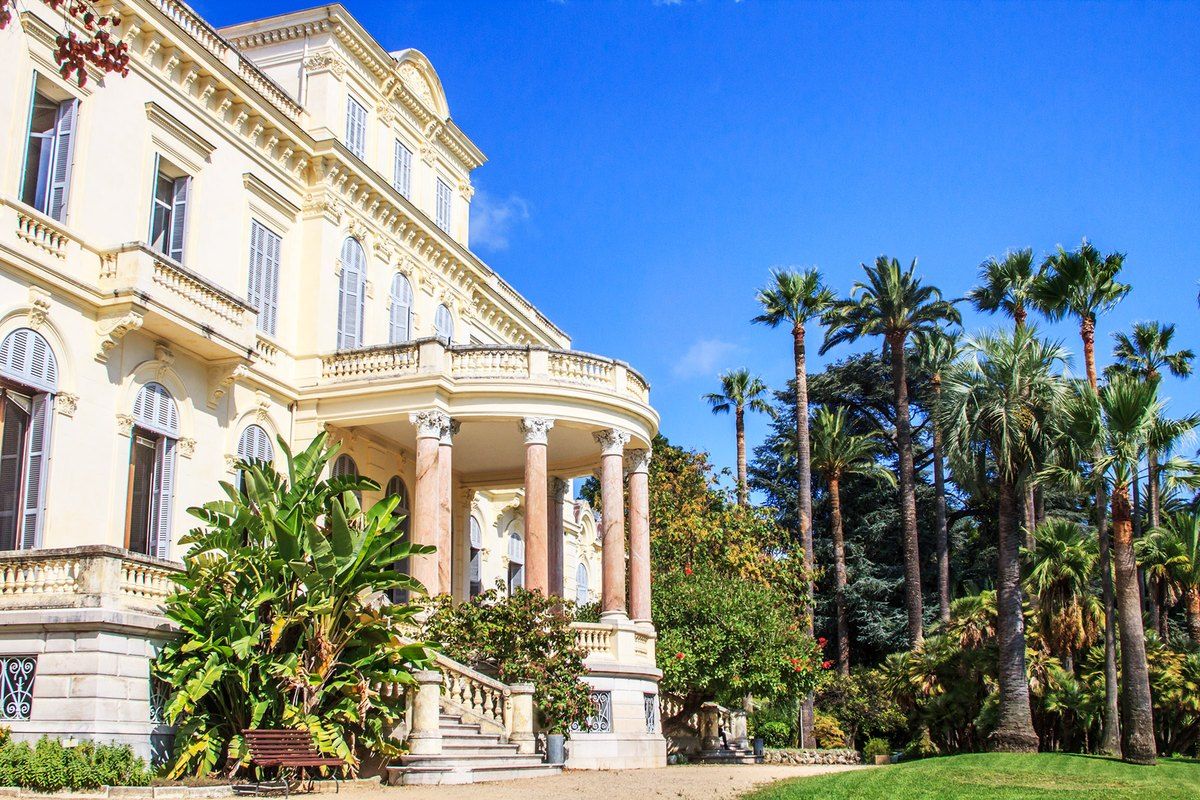 The neoclassical Villa Rothschild in Cannes behind palms and its garden lawns