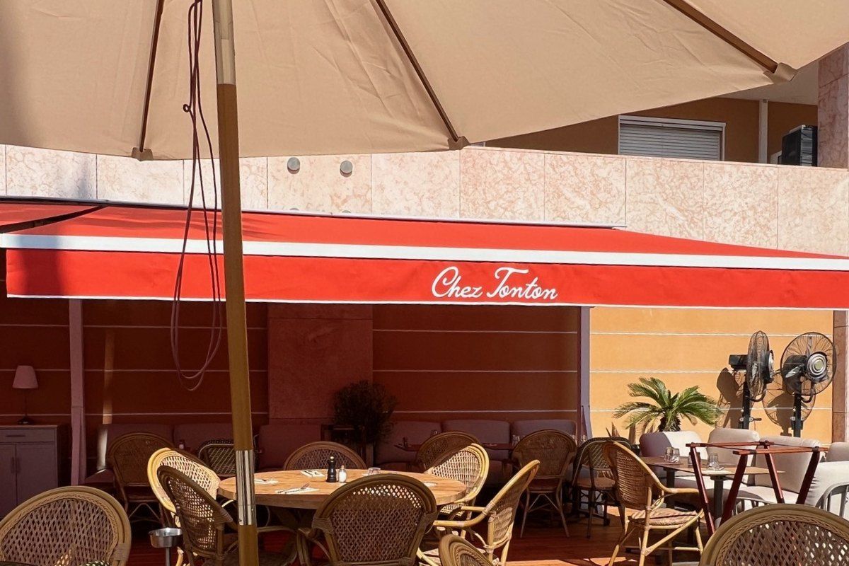 Rattan chairs on the terrace of Chez Tonton under its red awning at the port of Cap-d'Ail