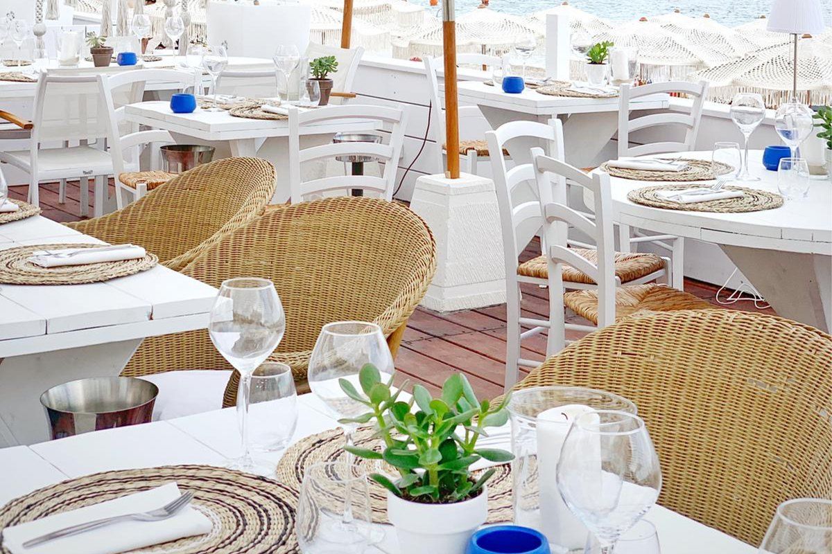 White tables, rattan chairs and parasols on the beach terrace of Naos Beach, Plage Marquet, Cap-d'Ail
