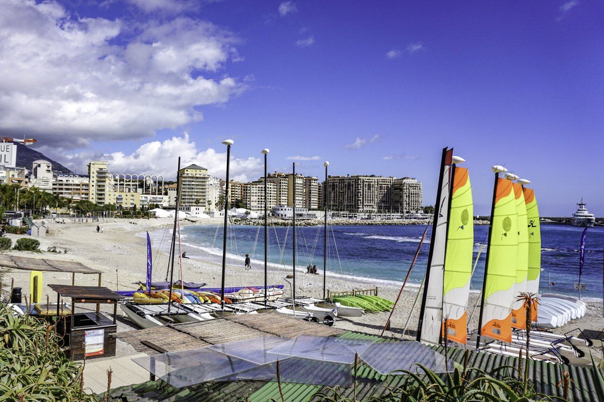 Small catamarans with bright sails drawn up on Plage Marquet, Cap-d'Ail, with Monaco's Fontvieille behind