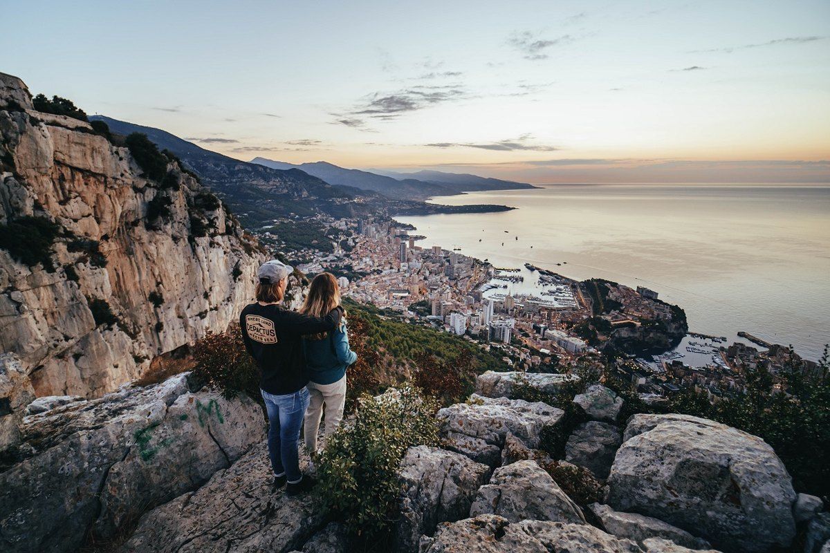 Two walkers on the white limestone of the Tête de Chien looking down on Monaco and the sea at dusk