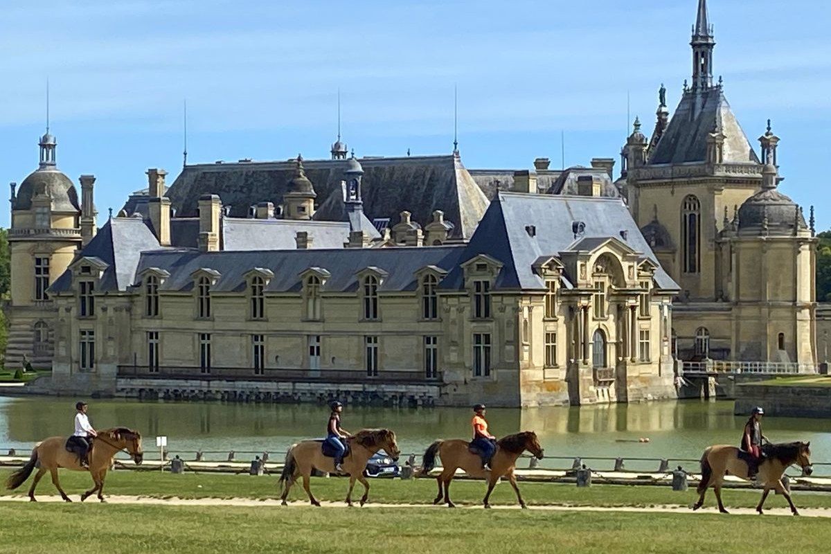 Riders on Henson horses crossing the lawn in front of the Château de Chantilly