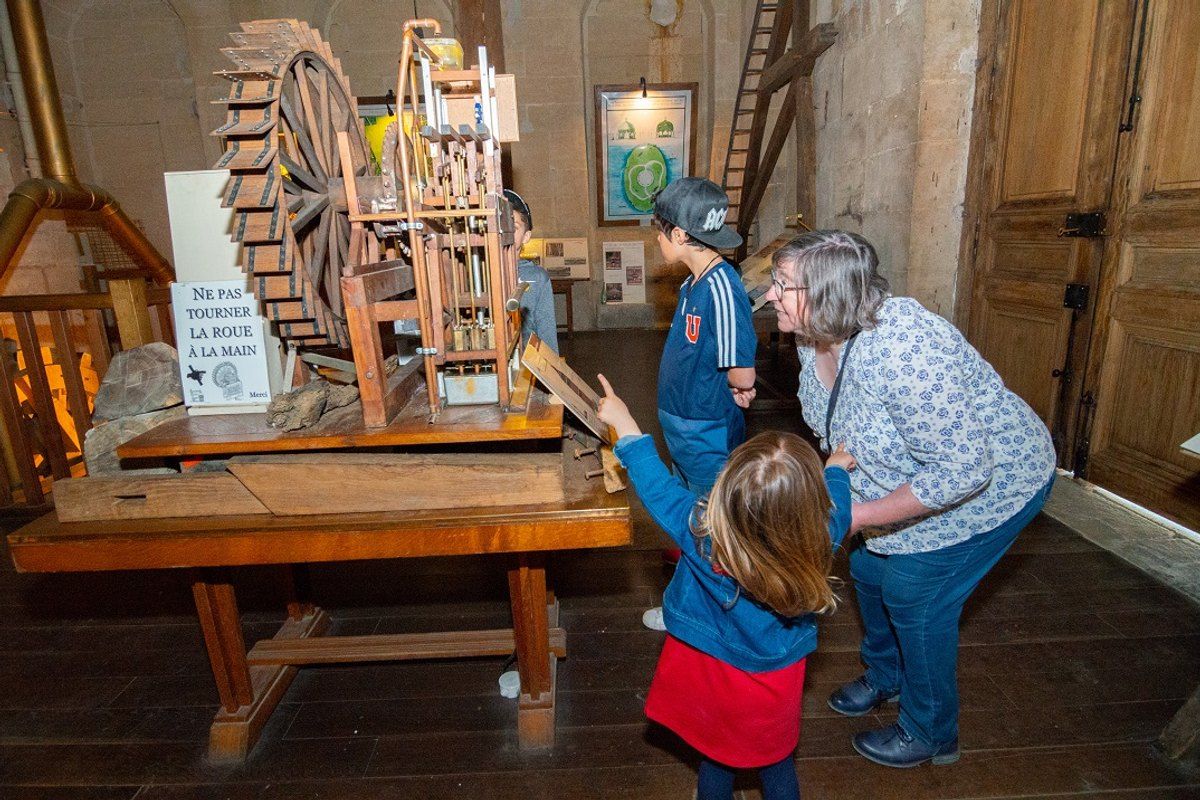 Children and a grandmother looking at a wooden water-wheel model at the Pavillon de Manse