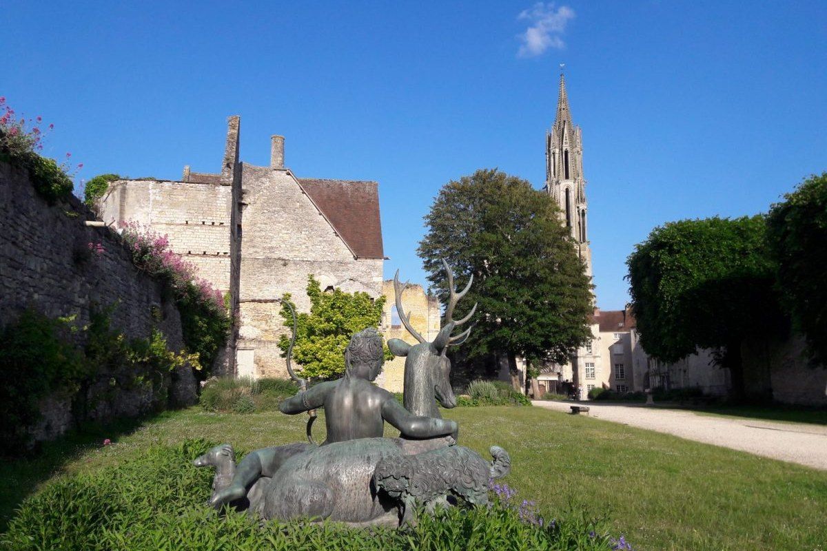 A bronze sculpture on the lawn of the château royal park in Senlis, with the cathedral spire behind