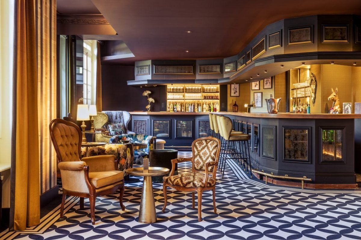 Velvet armchairs on a patterned floor before the bar counter of the Social Bar at Château Jeanne & The Forest