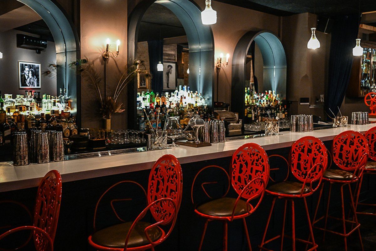 Red wrought-iron bar stools along the long counter under arched mirrors at Curfew cocktail bar on Vesterbrogade