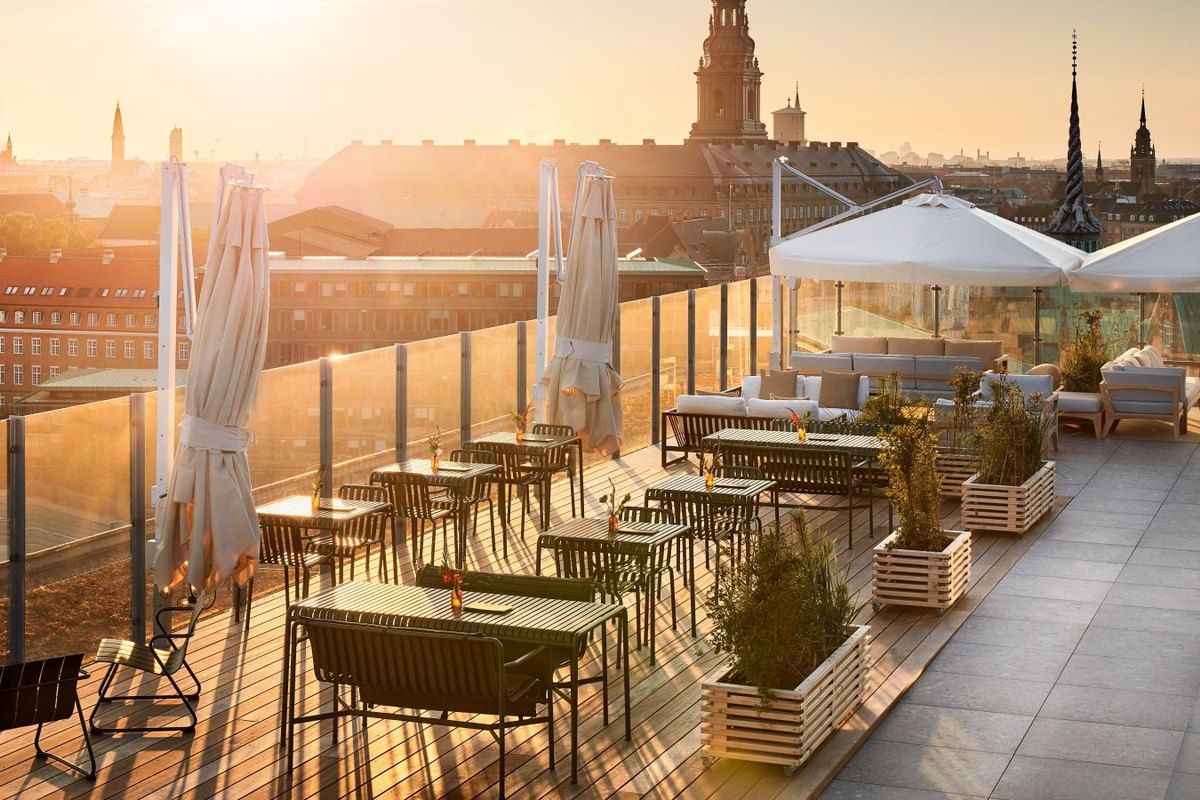 Tables and parasols on the ROOF terrace atop NH Collection Copenhagen in golden evening light, with the city's spires behind