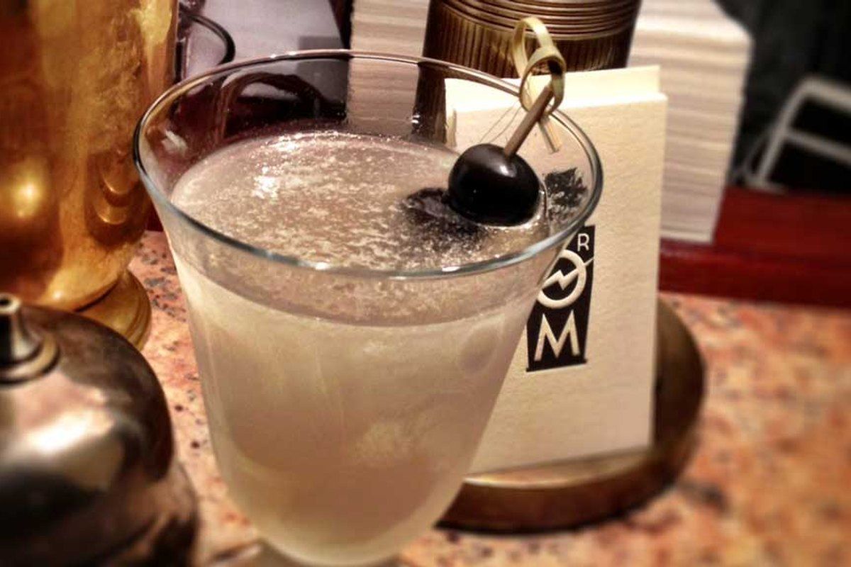A frosted cocktail with a cherry beside a Strøm Bar card on a marble counter