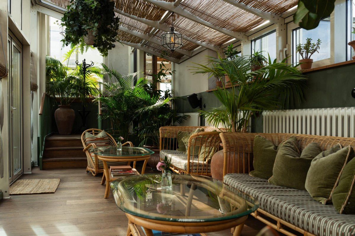 Rattan sofas, palms and a glass roof on the Sanders Rooftop terrace at Hotel Sanders