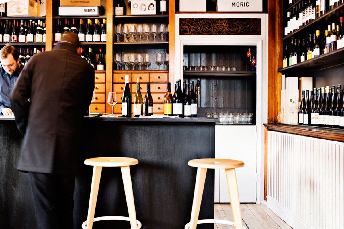 Wooden stools at the counter and wine-lined shelves inside Ved Stranden 10 wine bar and shop