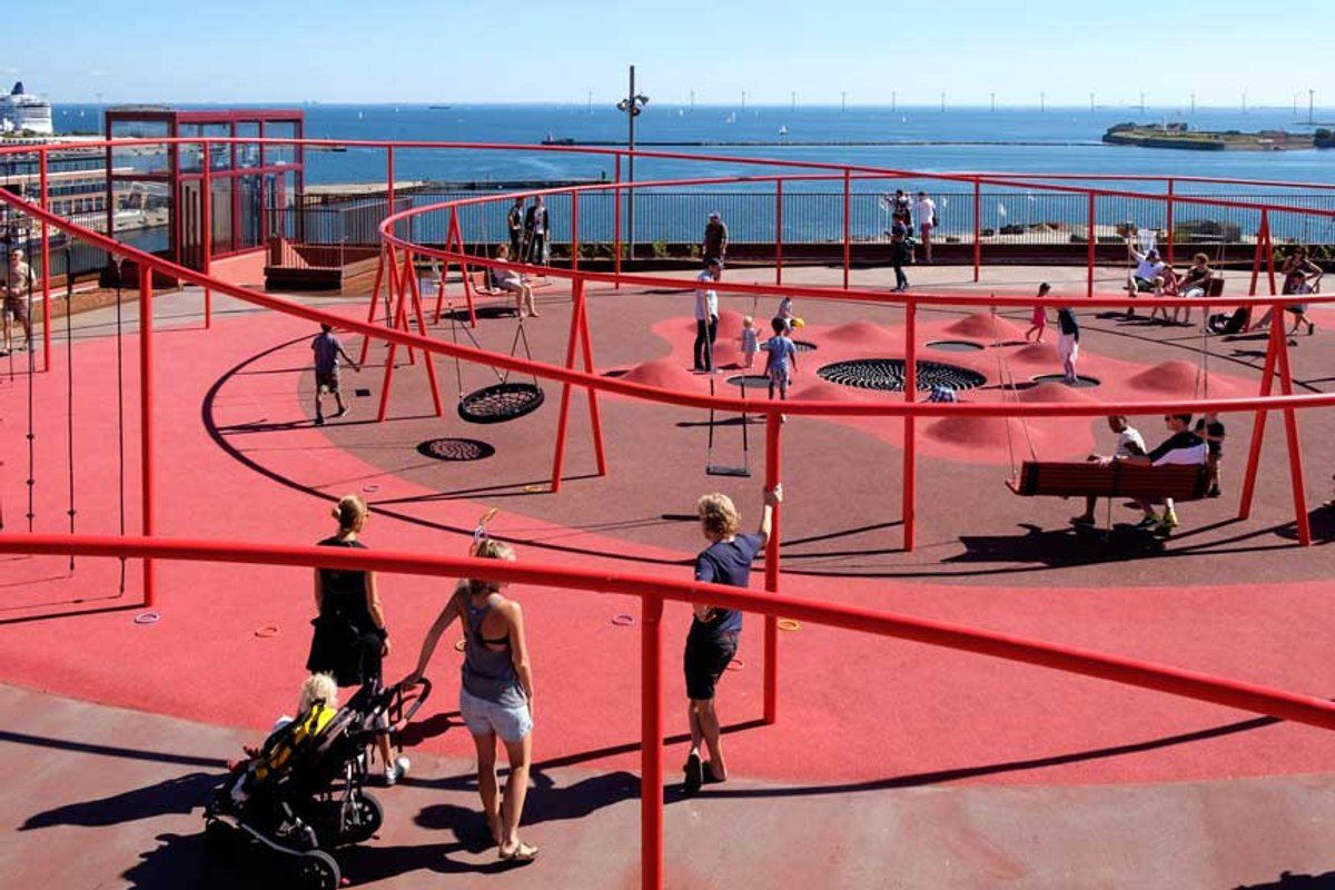 Families on the red rooftop playground of Konditaget Lüders in Nordhavn, with trampolines, swings and the sea beyond