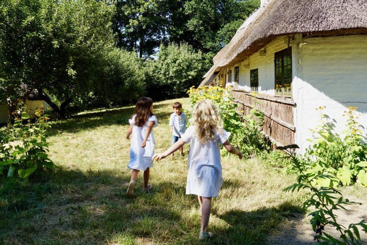 Two girls running across the grass beside a thatched, whitewashed farmhouse at the Open Air Museum in Lyngby