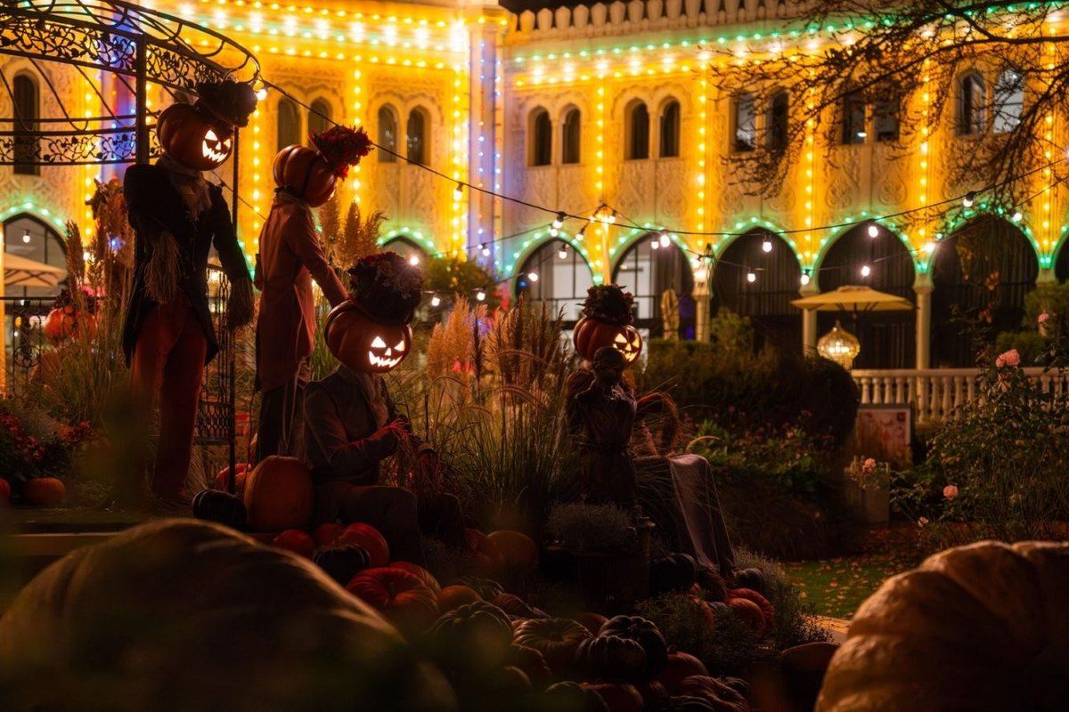 Halloween figures, pumpkins and strings of lights in front of the illuminated Moorish-style buildings of Tivoli Gardens at dusk