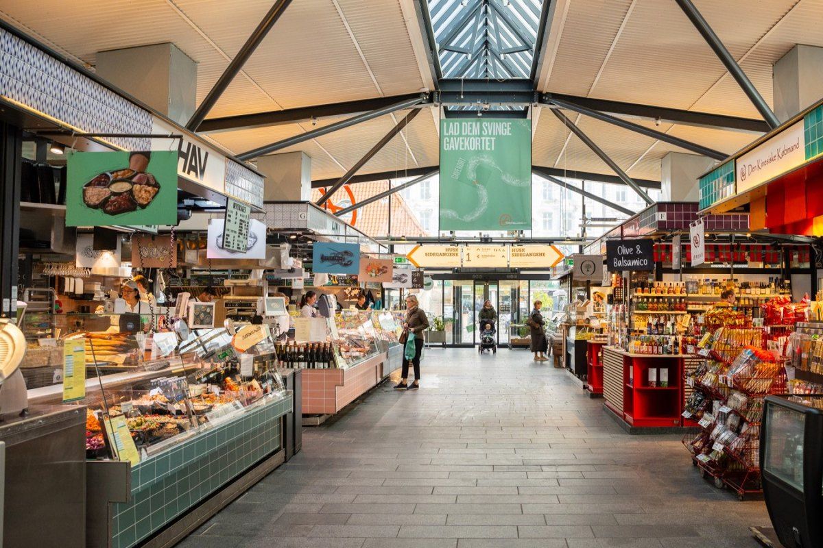 Food stalls and counters lining the central aisle of a Torvehallerne market hall in Copenhagen