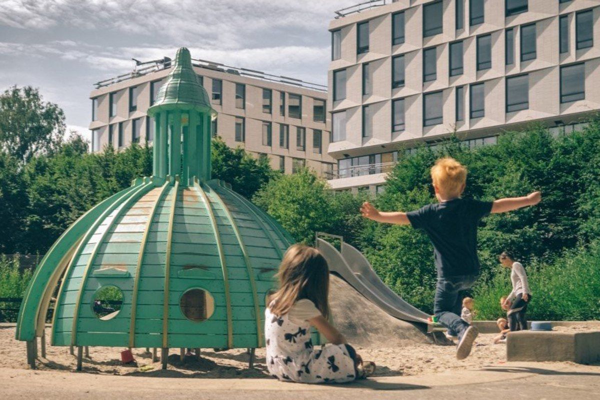 Children playing on a green copper-dome climbing frame modelled on a Copenhagen spire at the Tower Playground in Fælledparken