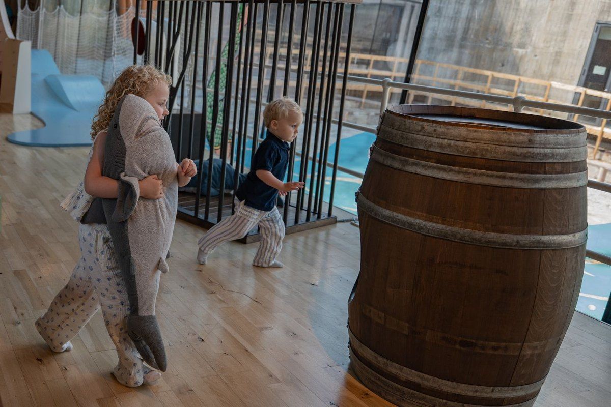Children running past barrels on the wooden deck of the Dream Ship play area at the M/S Maritime Museum of Denmark