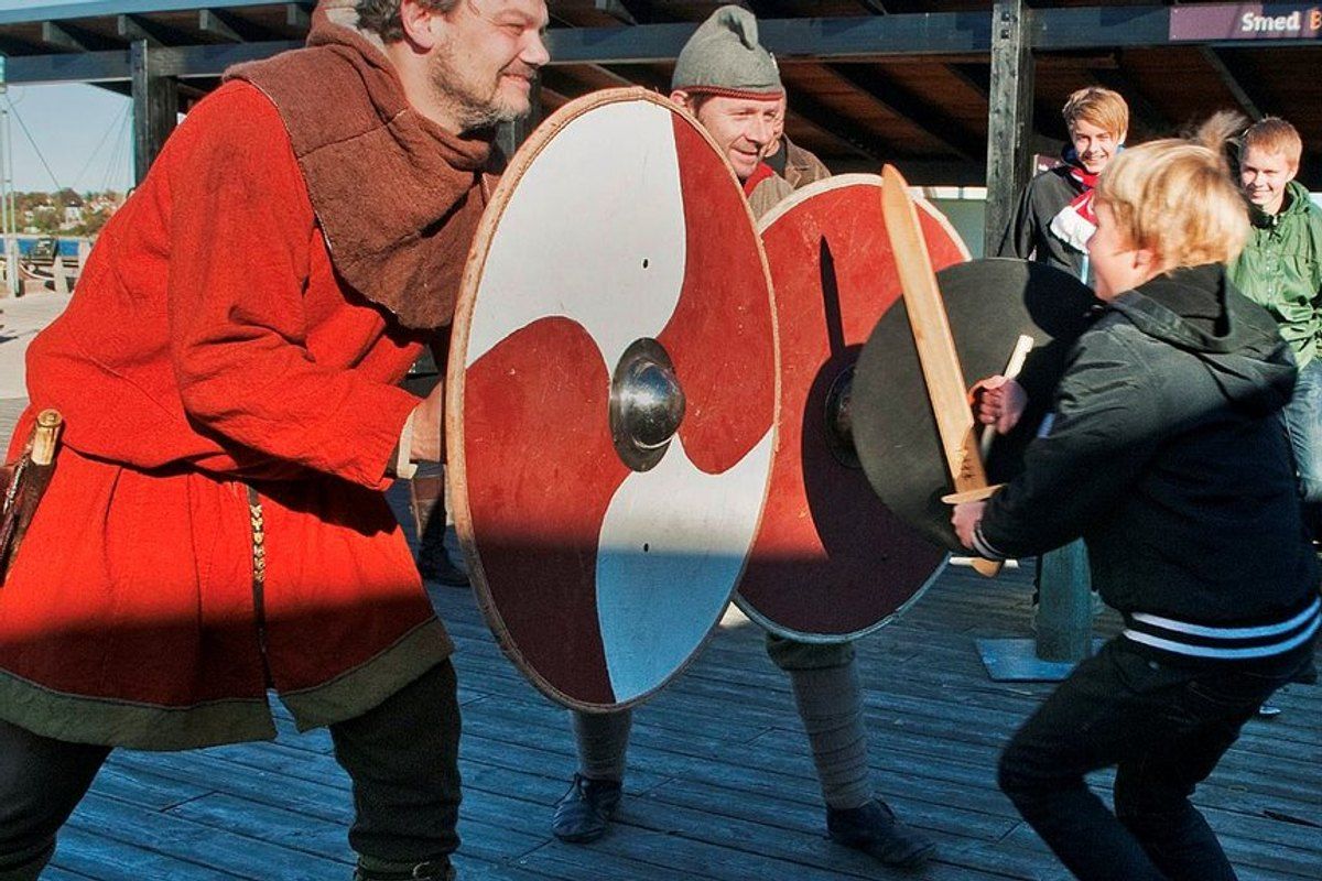 A man in Viking costume teaching a child to fight with a painted wooden shield at the Viking Ship Museum in Roskilde