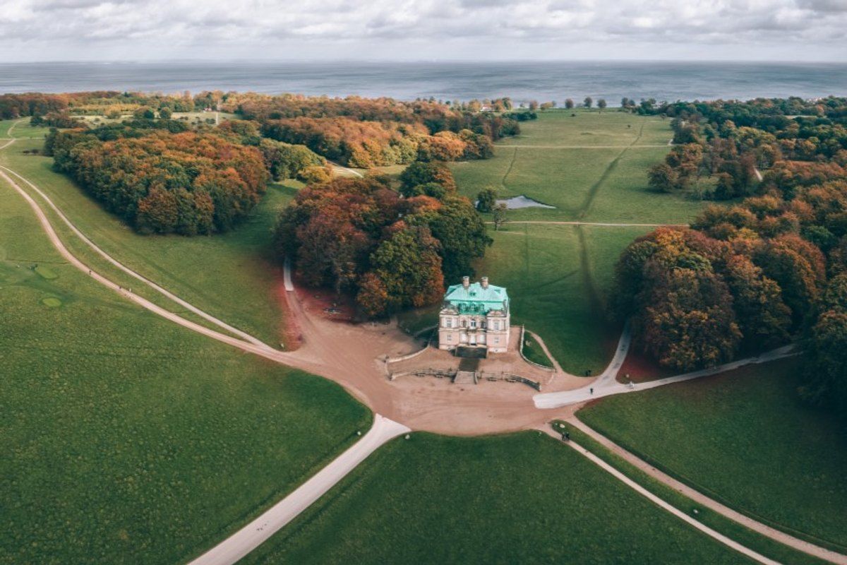 Aerial view of the Hermitage hunting lodge in Dyrehaven, its open plain ringed by autumn woods, with the Øresund beyond