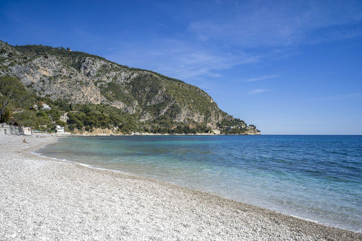 The pebble beach of the Baie d'Èze at Èze-sur-Mer, with the clear sea and the coast beyond