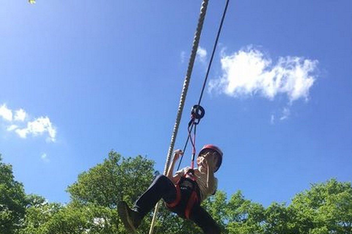 A child in a helmet hanging from a zip line high in the trees at L'Accro des Arbres, Bois-le-Roi