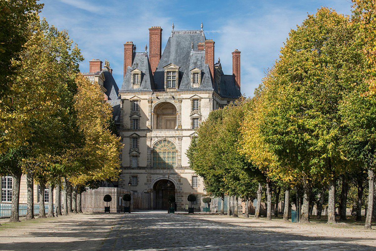 An avenue of autumn trees leading to a Renaissance gate pavilion of the Château de Fontainebleau