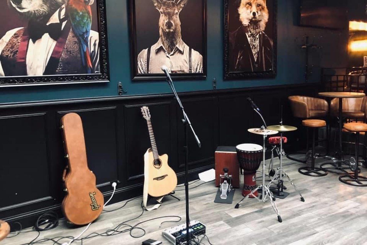Guitars, a microphone and drums on the small stage under animal portraits at Le Castle Pub, Fontainebleau