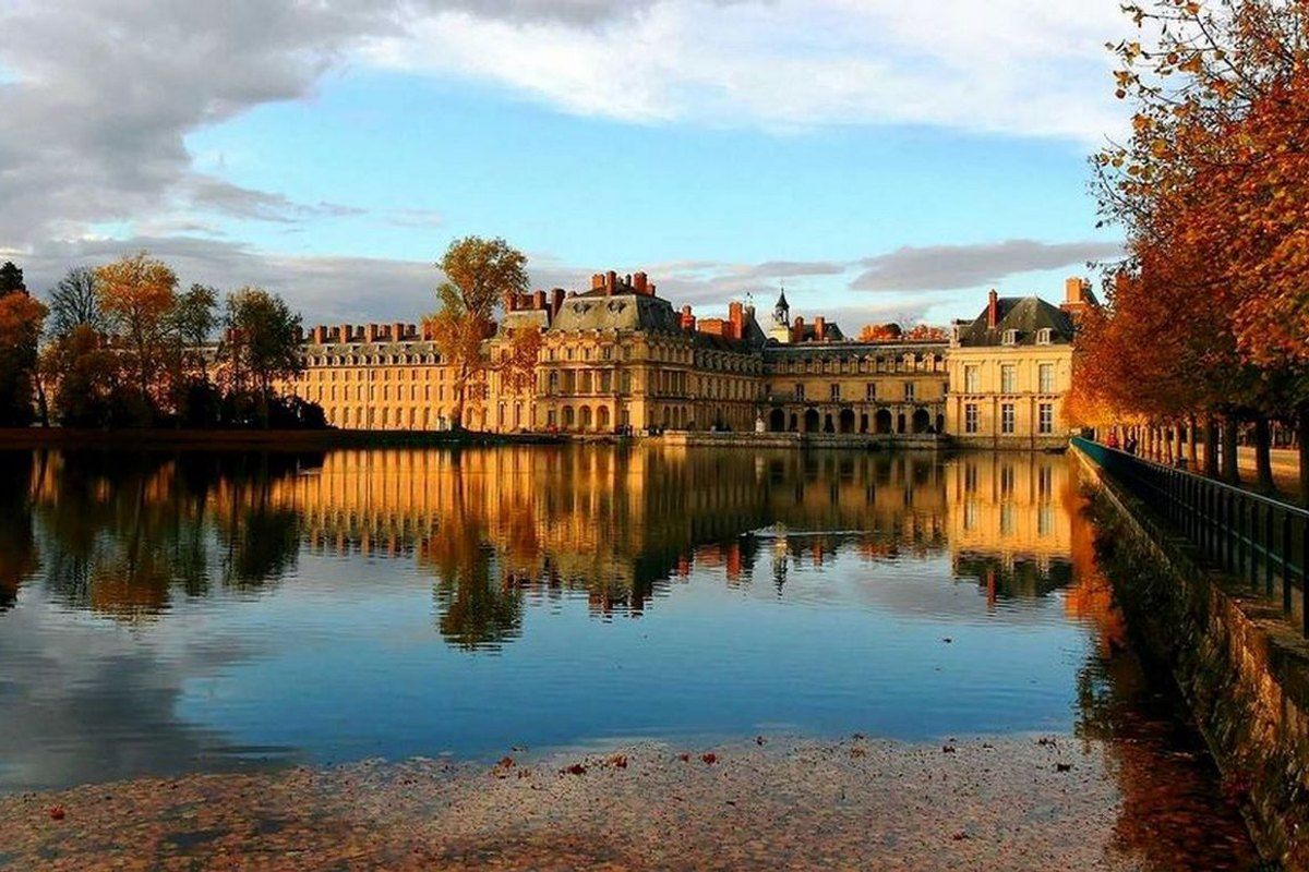 The Château de Fontainebleau reflected in still water with copper autumn trees along the bank