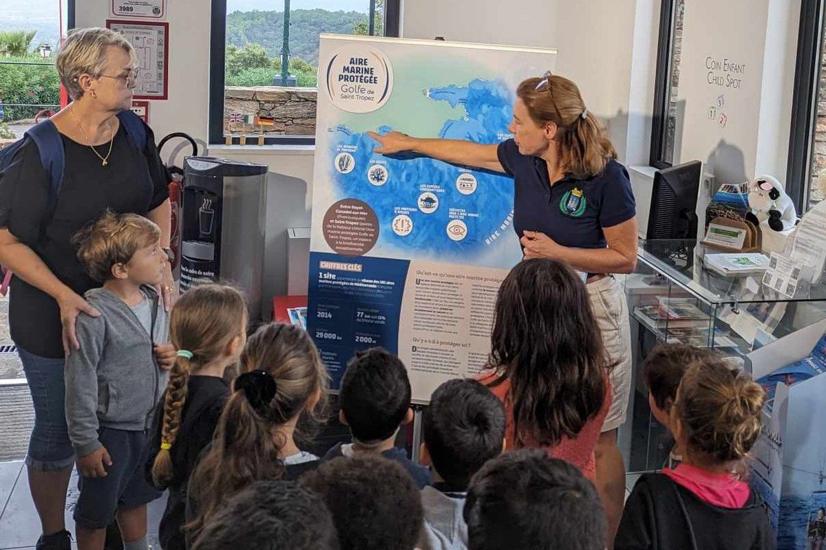 Children gathered round a guide and a map display inside the Gassin tourist office