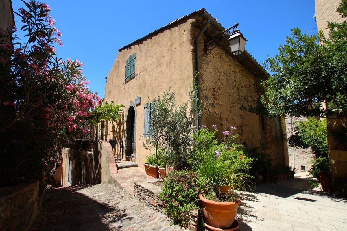 The Barbacane, an old stone house with blue shutters among flowers in the medieval village of Gassin