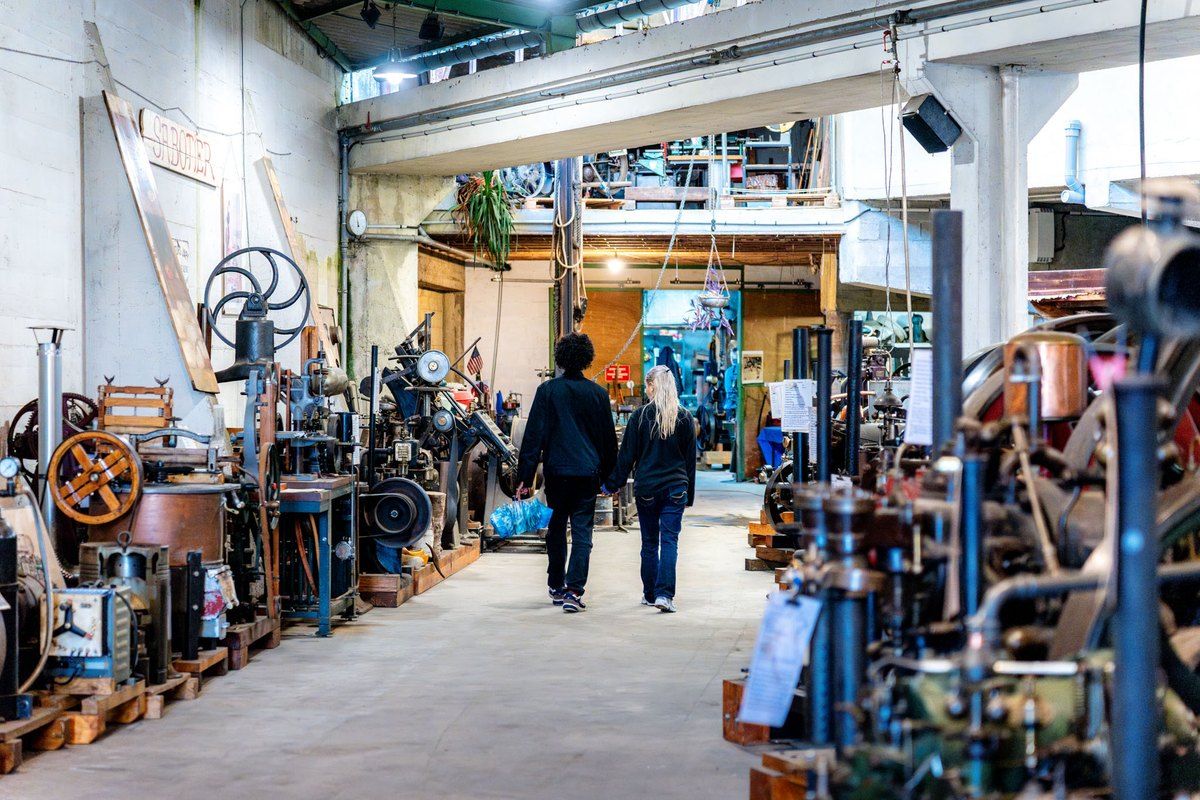 Visitors walking between restored engines and machines in the Musée de la Mécanique Naturelle, Giverny