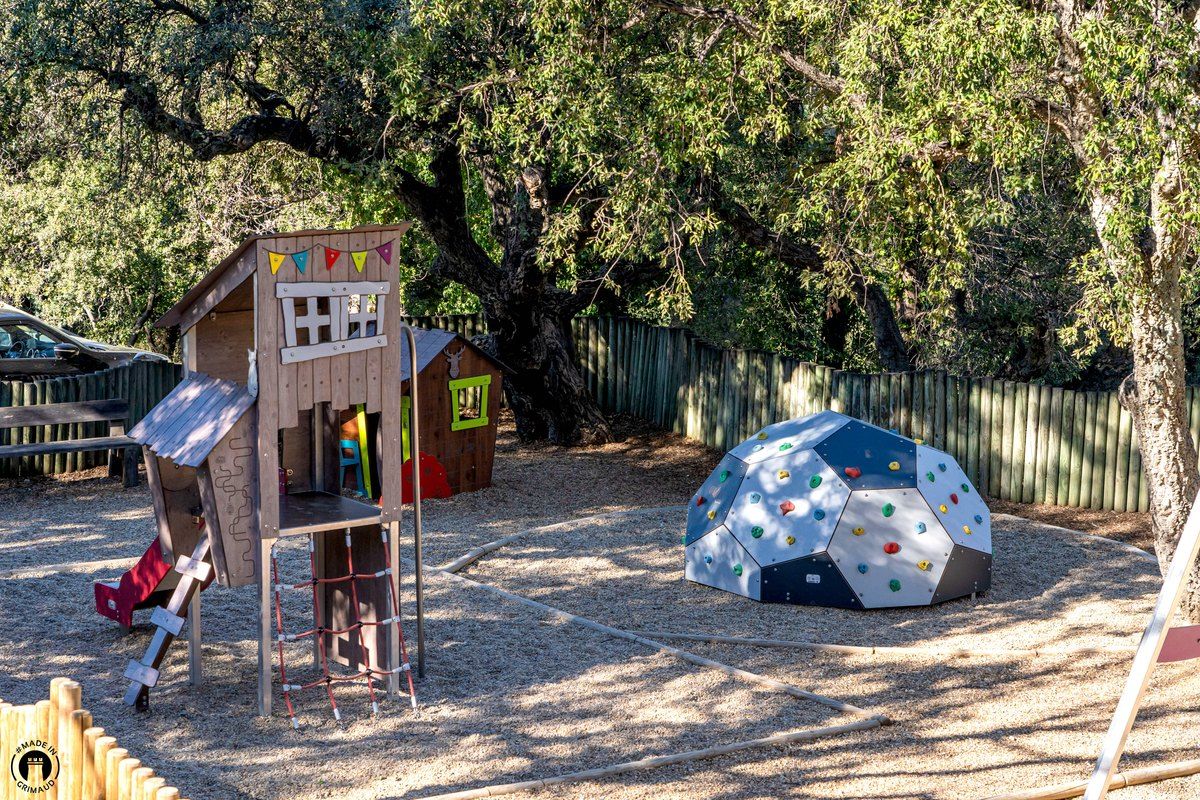 Wooden play house with a slide and a climbing dome under the oaks at the castle playground in Grimaud