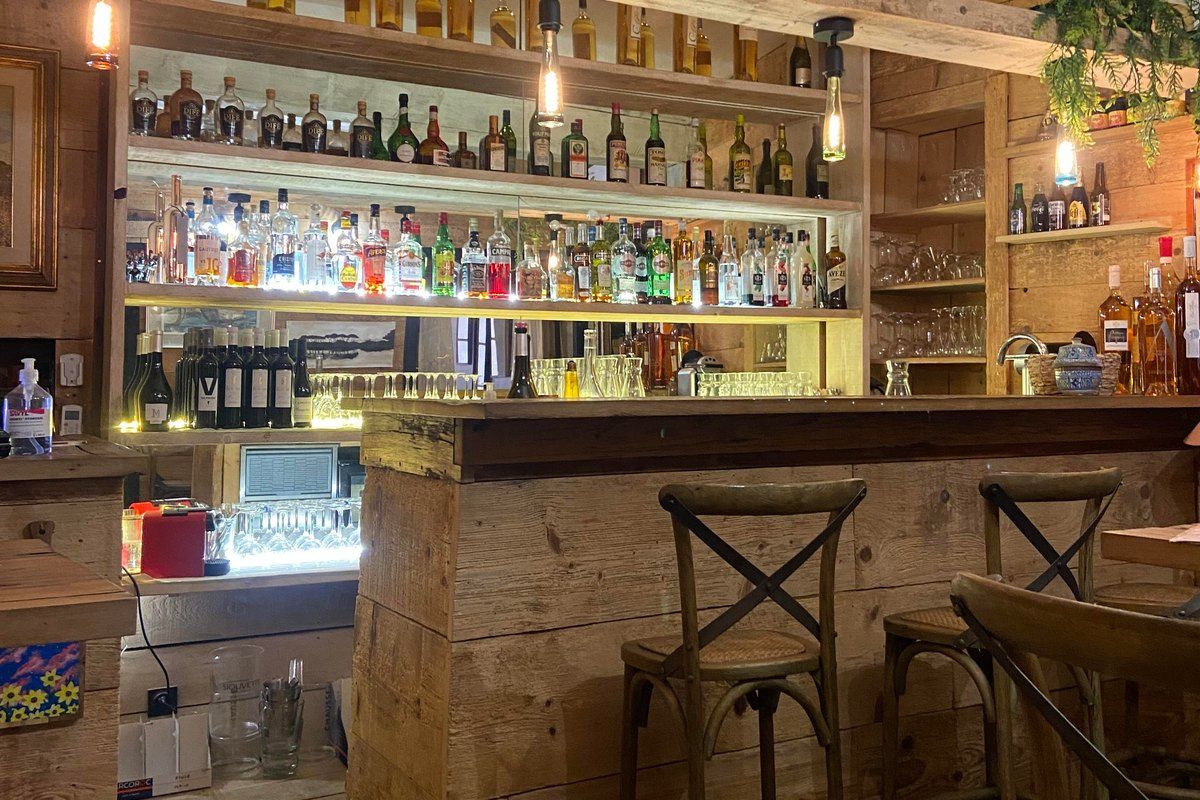 Bar stools at the wooden counter of Art & Bar, shelves of bottles lit behind