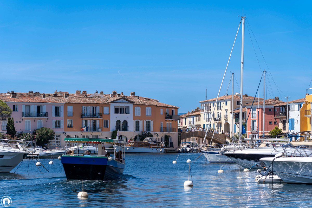 A canopied water-bus boat crossing the harbour in front of the pastel houses of Port Grimaud