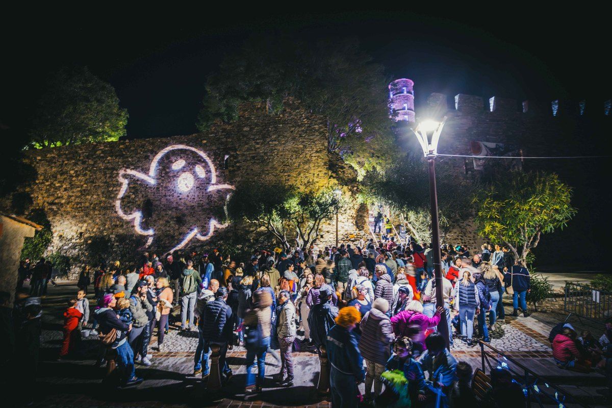 Families in costume gathered below the floodlit castle walls of Grimaud on Halloween night, a ghost projected on the stones