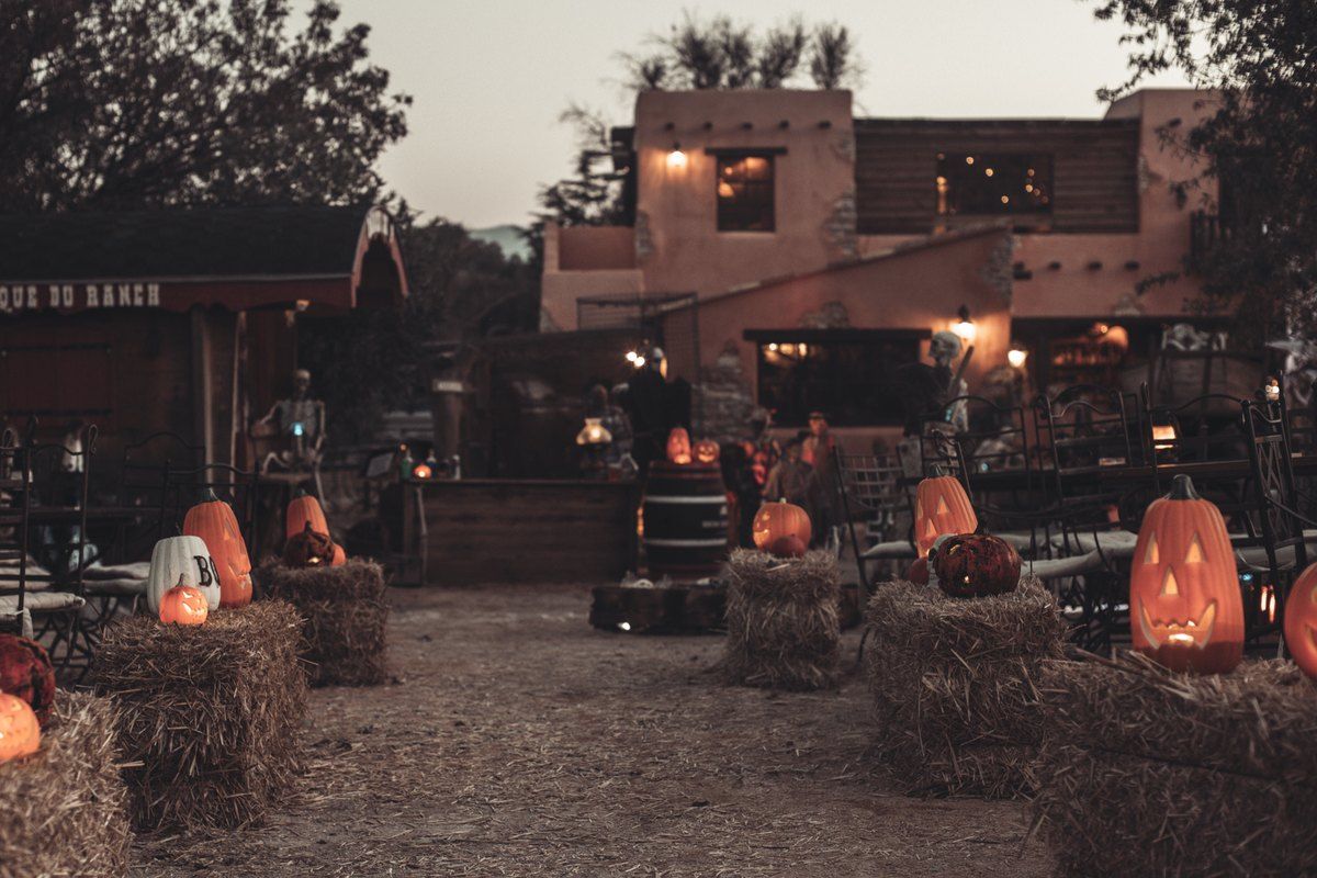 Carved pumpkins and straw bales in the yard of the Ranch La Mène at dusk, decorated for Halloween