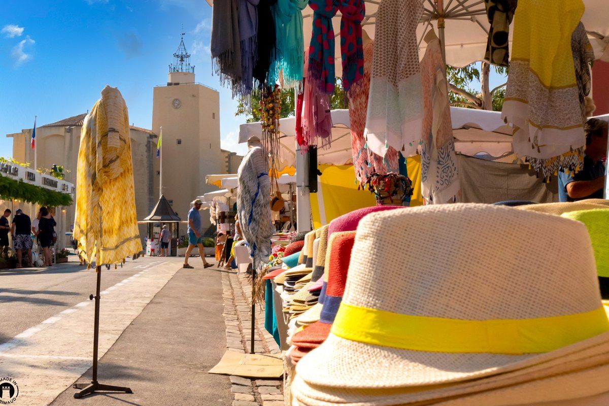 Straw hats and linen on a market stall in Grimaud village, the church tower behind