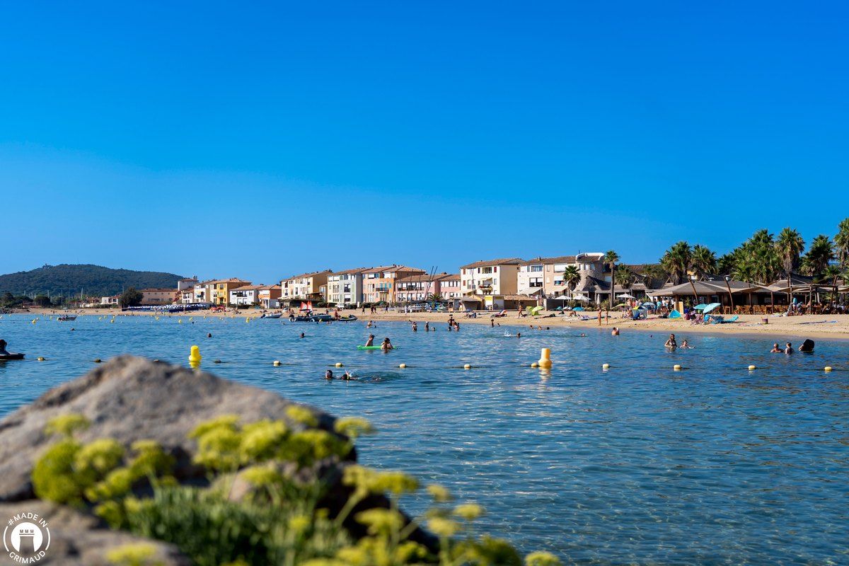 Swimmers in the calm water off the sandy Plage de Port Grimaud, with the houses of the lagoon town behind