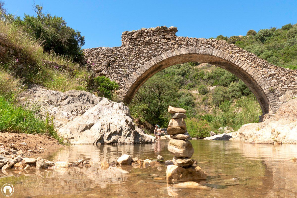 The stone arch of the Pont des Fées over the clear water of the La Garde stream, a little cairn in the riverbed