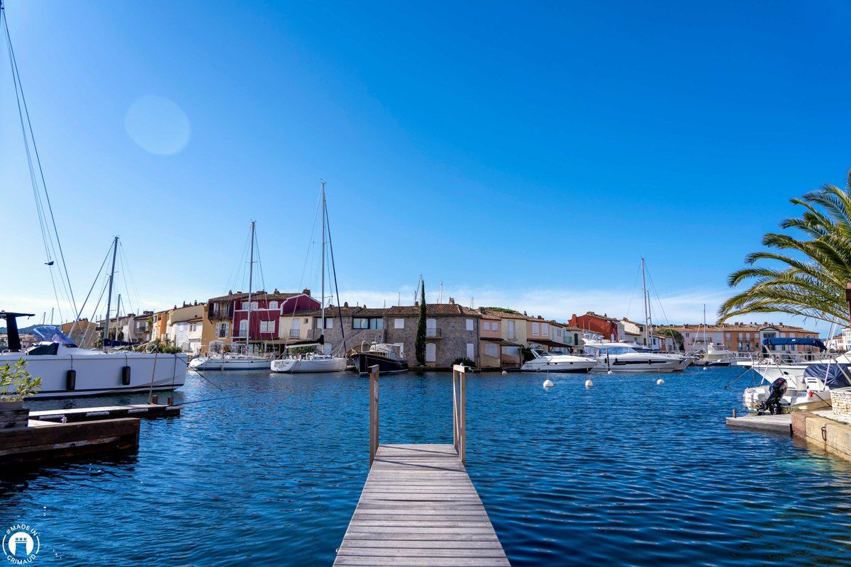 A wooden pontoon running into the calm harbour of Port Grimaud, the houses and masts across the water