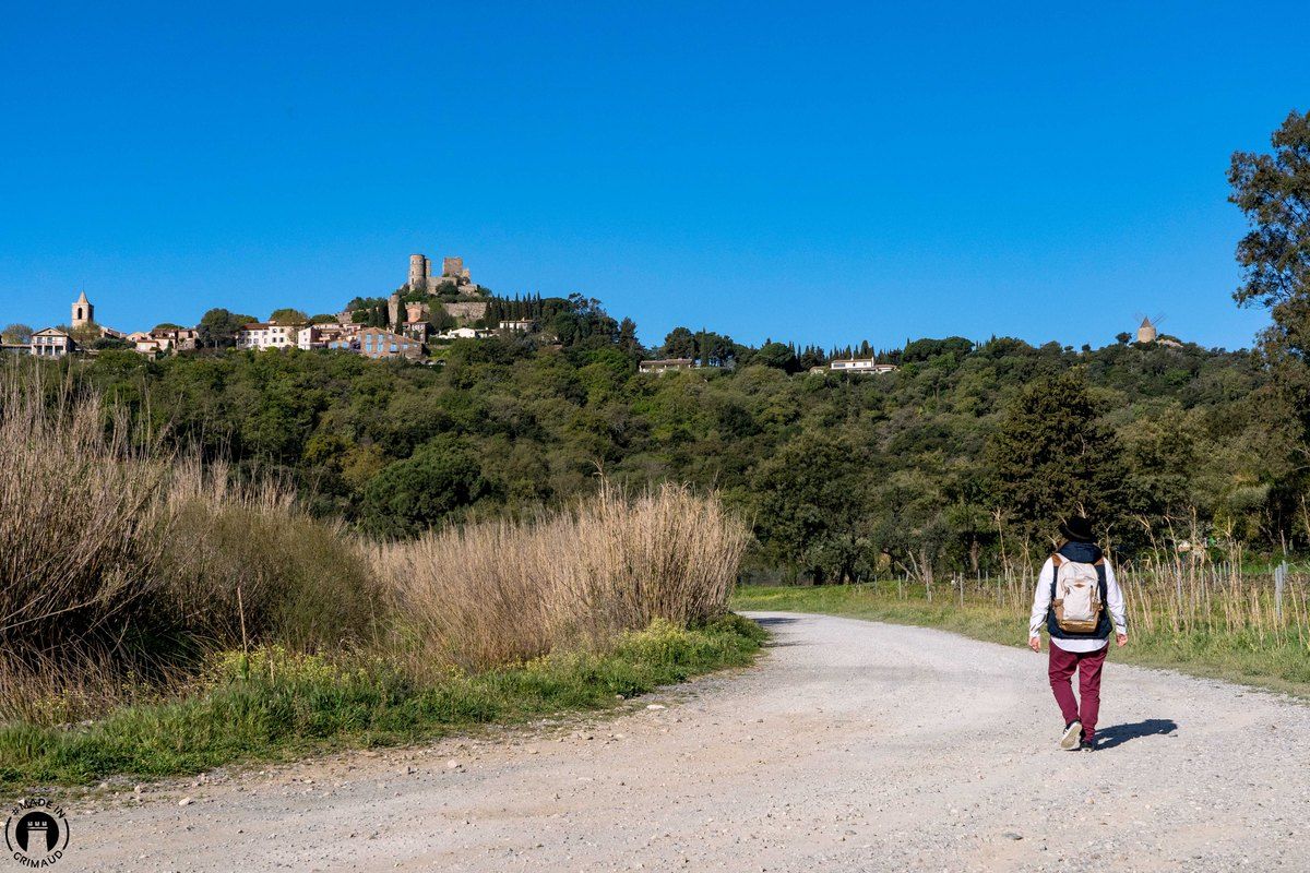 A walker on a gravel track through the hills, with the village and castle of Grimaud on the skyline