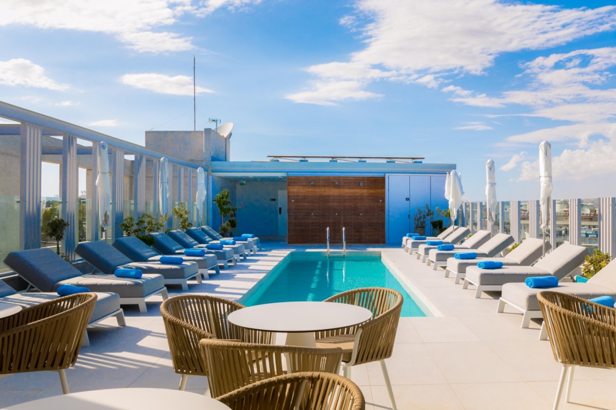The Kampana rooftop pool at Hotel Indigo Larnaca, with sunbeds, parasols and rattan chairs under a blue sky