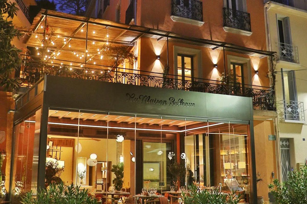 La Maison Bellevue lit up at night, with festoon lights over its glass-fronted terrace on Place Bellevue